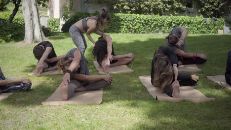 Yoga-trainer-helping-people-stretching-in-park